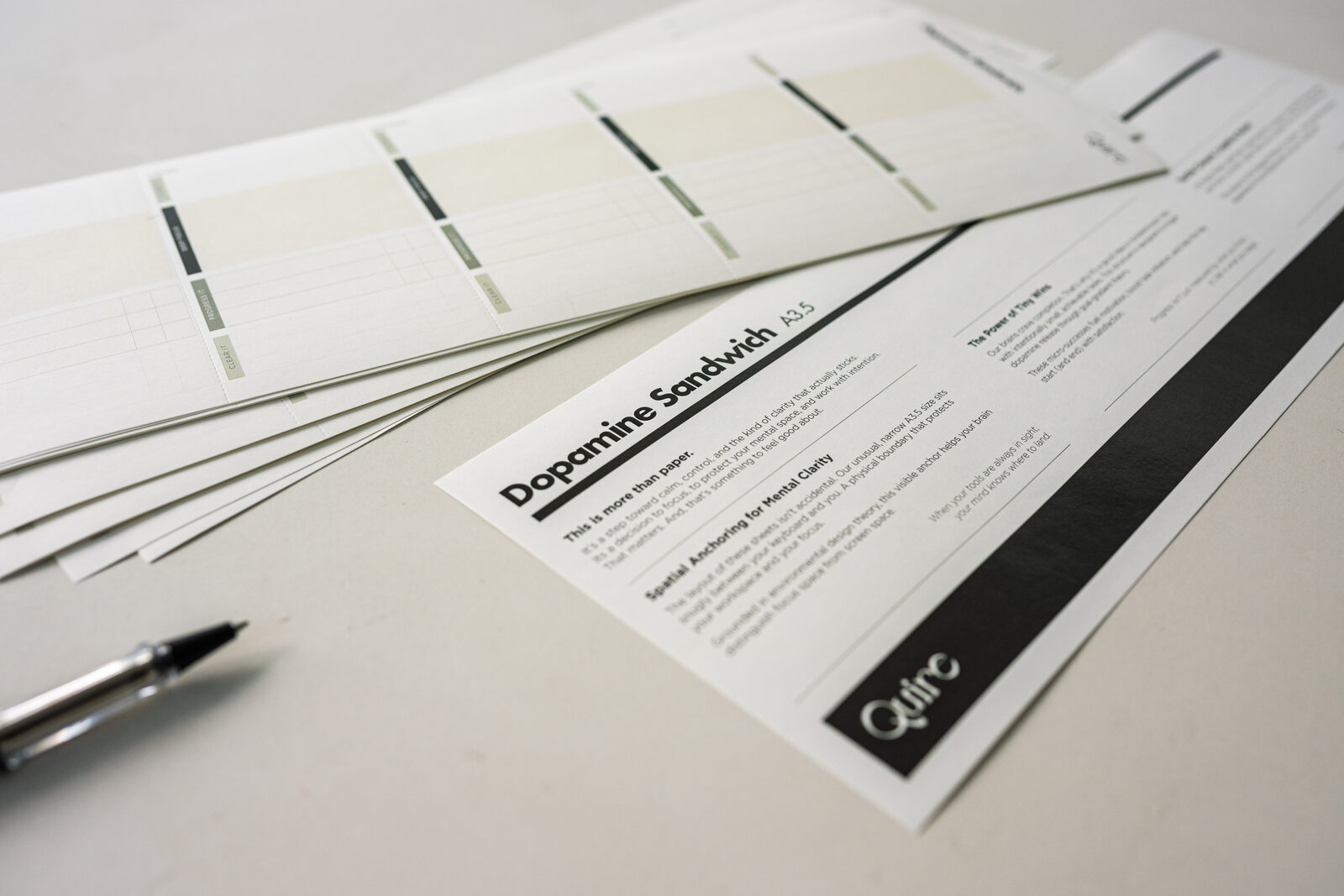 Quire planner pages fanned out beside the printed cover sheet and a pen